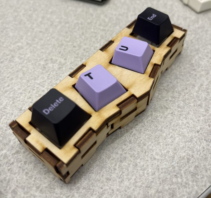 Three-dimensional slanted rectangular box with holes cut-out. Design reflects the SolidWorks design, keycaps added onto the mechanical switches- Completed fidget toy.