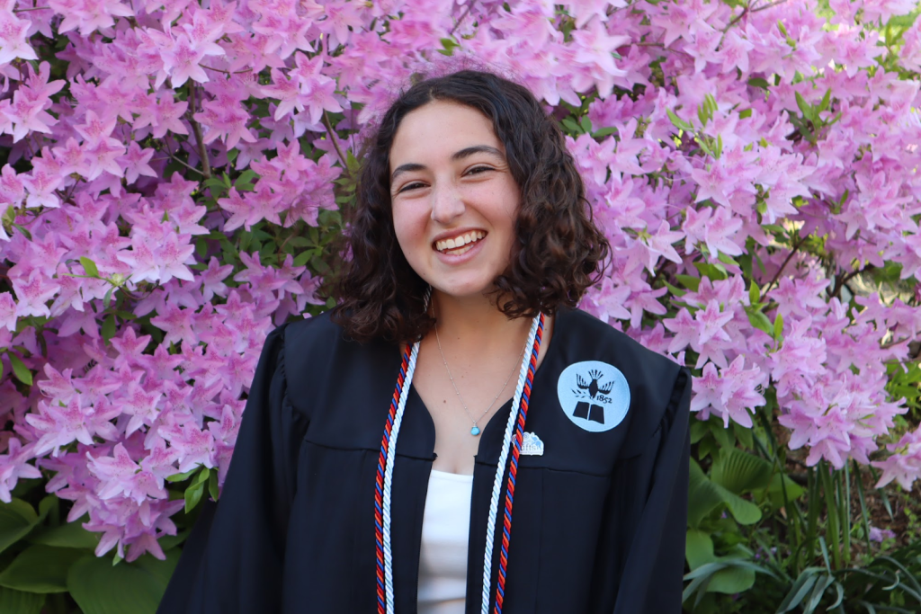 Sophie Hankin in graduation regalia in front of purple flowers