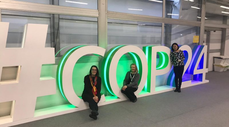 Mieke, Kelly, and Fang standing in front of the COP24 sign, which is illuminated with green and blue lights