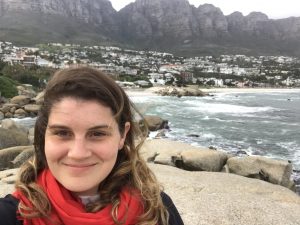 Elizabeth Minchew selfie standing on rocks by the shore, with a bay, beach, and city in the background