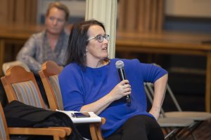 Photo of Kelly Sims Gallagher leaning back in a chair, speaking into a microphone