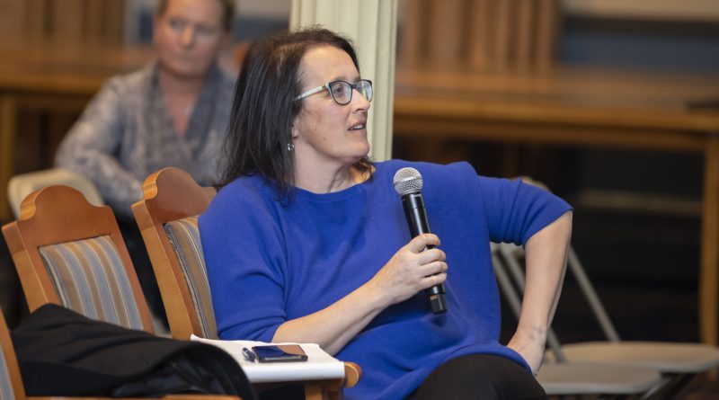Photo of Kelly Sims Gallagher leaning back in a chair, speaking into a microphone