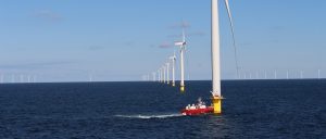 Photo of offshore wind turbines and a red boat at the base of the first turbine in the foreground