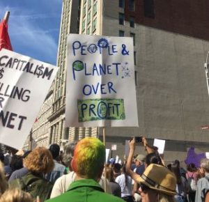 Photo of sign at a protest that reads "people and planet over profit"