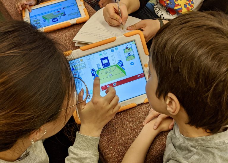 An undergraduate student, enrolled in a course investigating technology tools for playful learning, shows one of our curious learners how the Scratch Jr. app works.