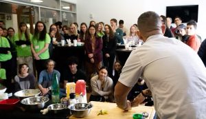 A man presenting a food preparation demonstration to a group of people 