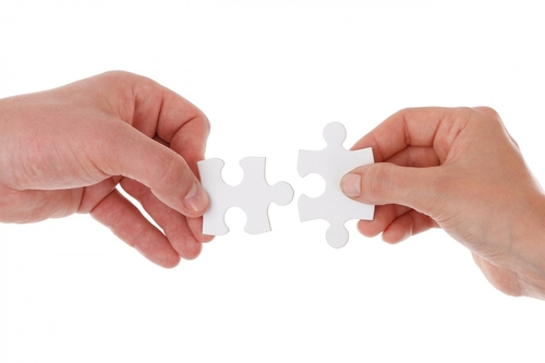 two hands fit puzzle pieces together