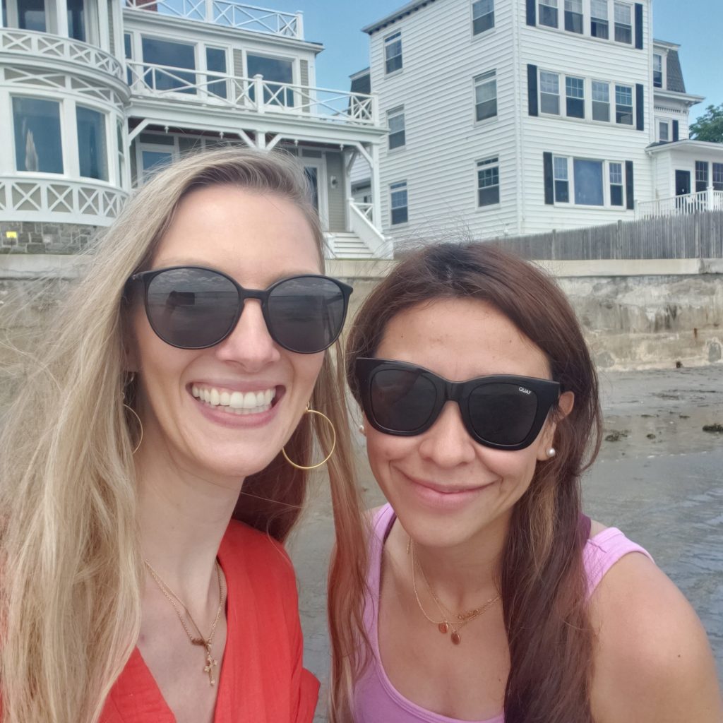 Melissa D. and Cynthia C. take a selfie photo together in front of a beach house. 