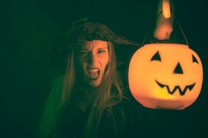 Woman dressed as a witch holding a lighted pumpkin