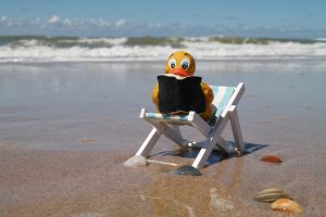 Rubber duck reading a book in lounge chair on the beach