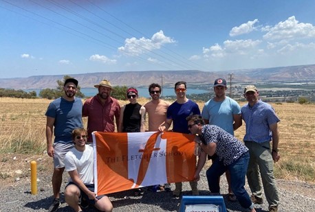 Group of Fletcher School students holding an orange and white Fletcher School flag at the Noah Kinarti Observation Point.