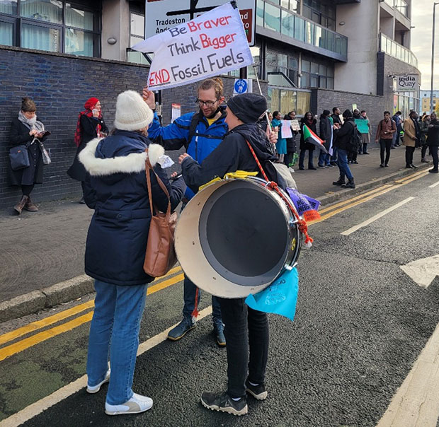 Three protesters stand on the street with signs in their hands.