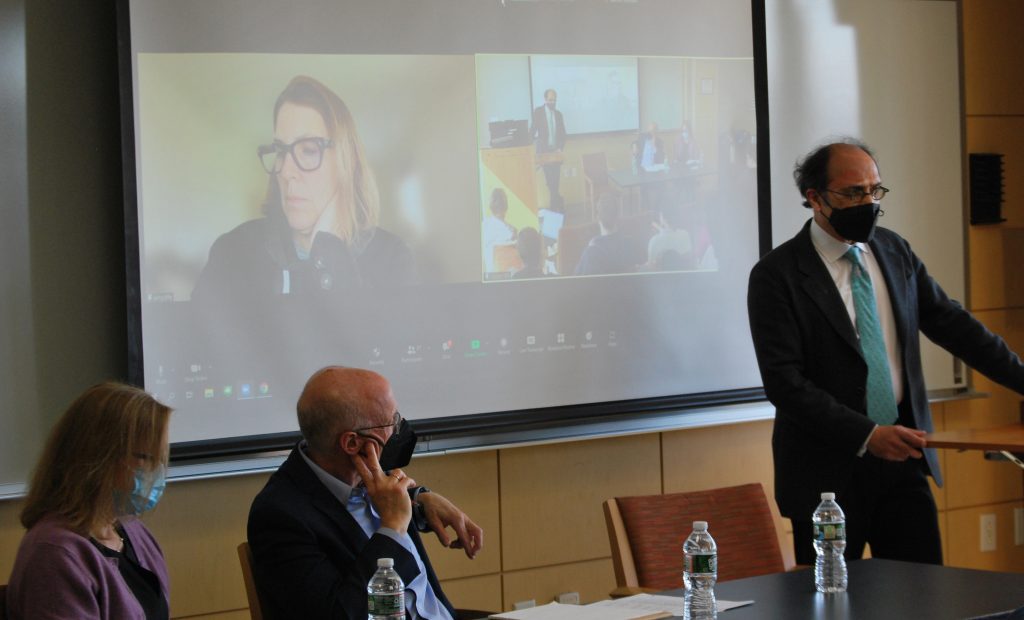 Monica Toft,, Joel Trachtman, sitting at a table, Amy Myers Jaffe, (onscreen), and Bhaskar Chakravorti standing a podium