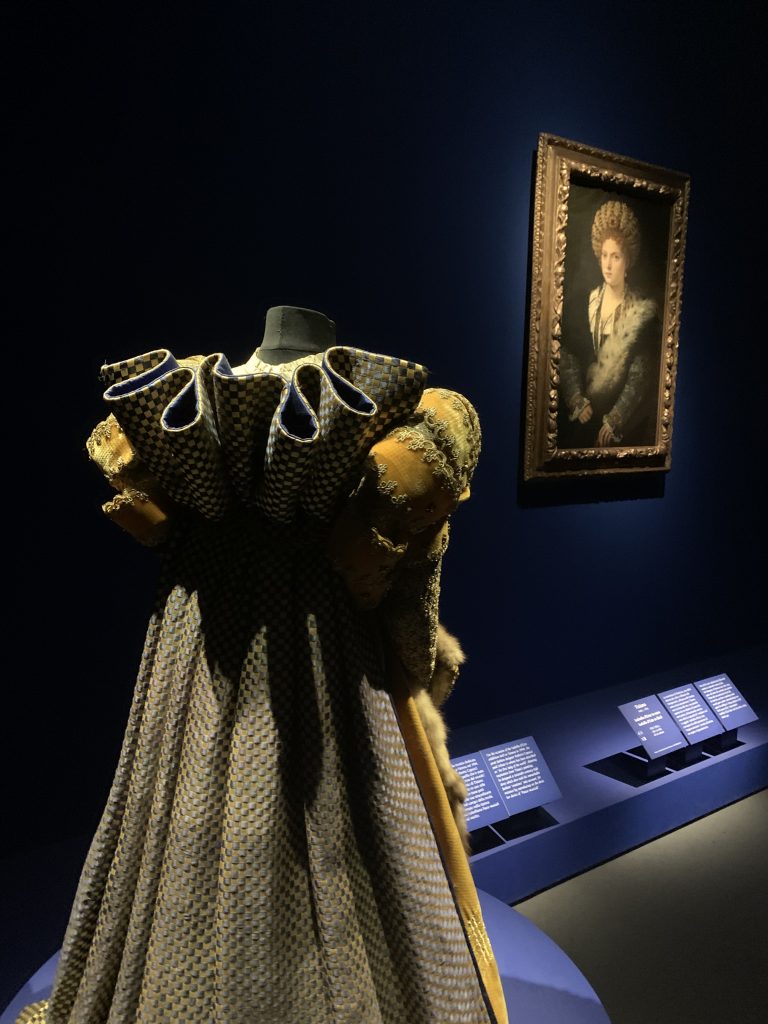 a small, gold and blue Renaissance dress seen from the back, facing Titian's portrait of Isabella d'Este