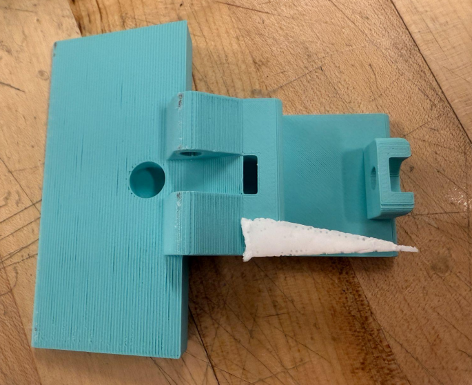 One half of our device, shown in teal, laid out on a table. The wedge of opening mechanism is made with white polyurethane. The photo is taken from a top-down view.