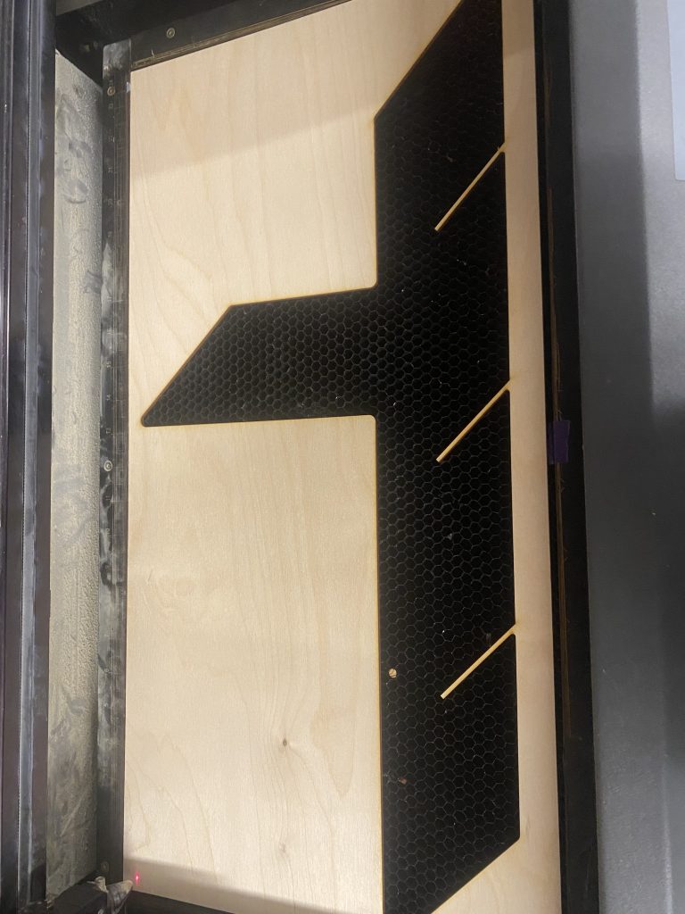 A piece of birch wood on the bed of a laser cutter after laser cutting one leg.