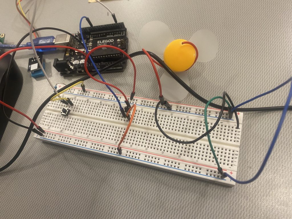 Picture includes a breadboard involving wires and connected to the UNO R3 Controller Board with wires. Press Button and Fan Motor are also connected to breadboard.