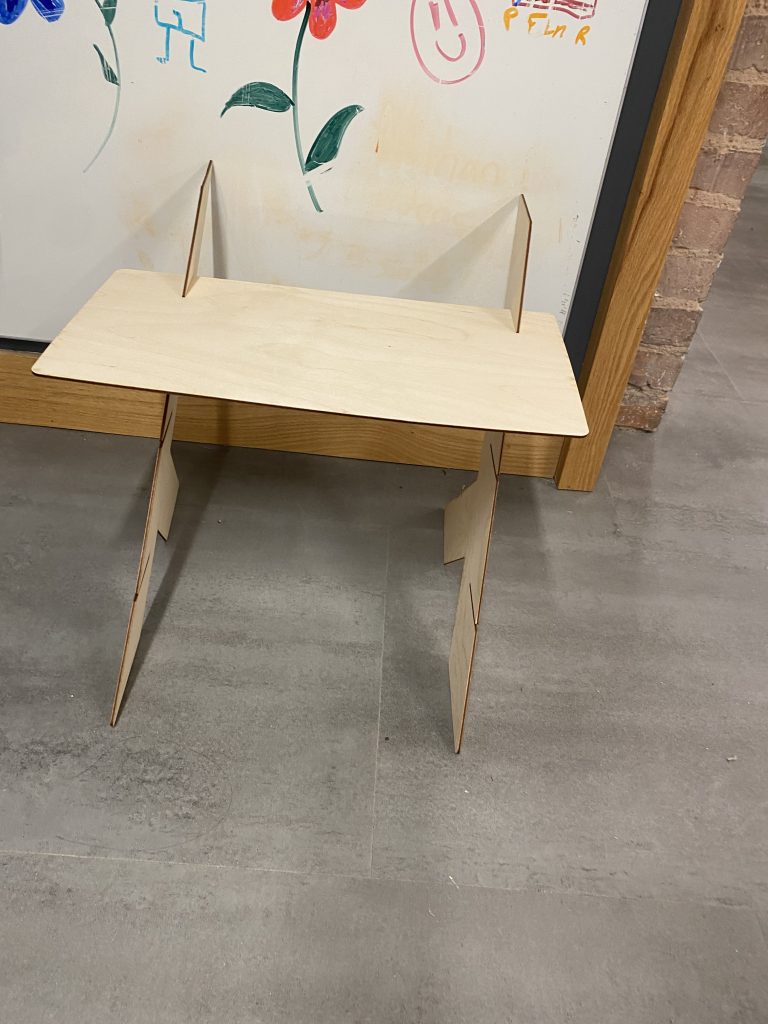 2 pieces of standing legs with one shelf at the top sat in the ground leaning on a whiteboard.