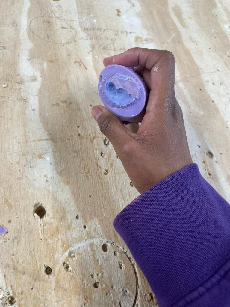 Picture including casted object in purple silicone to the shape of the mold (elliptical shape), top view.