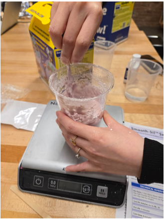 Picture including a cup on a scale while mixing pink molding material (alginate).
