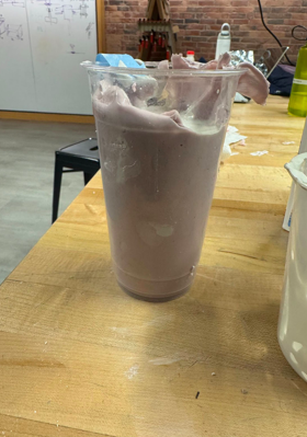 Picture including a cup on a wood table with a pink molding material where casting material (plaster of Paris) was poured.