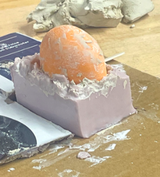 Picture including mold with divots and half bottom part of the orange 3d printed object showing.