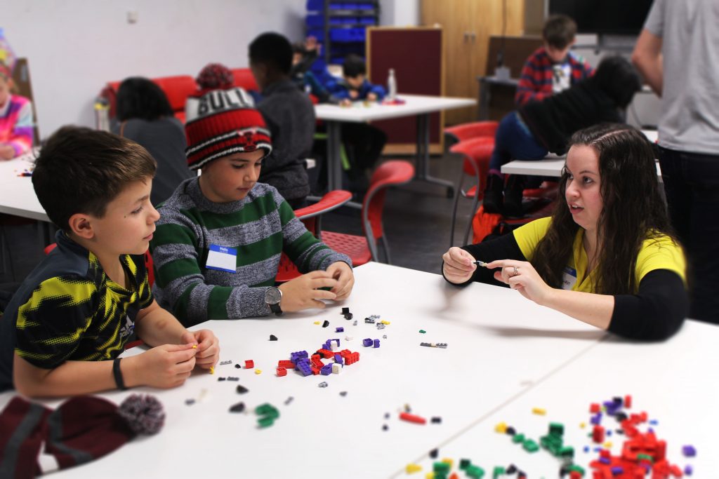 A young teacher kneeling at a table with two students. 