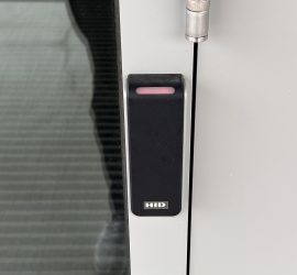 Black, rectangular ID card scanner next to the outside door of the Kelley Sim Lab with a red indicator light, showing that it is locked.