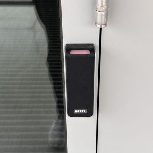 Black, rectangular ID scanner next to the outside door of the Kelley Sim Lab with a red indicator light, showing that it is locked.