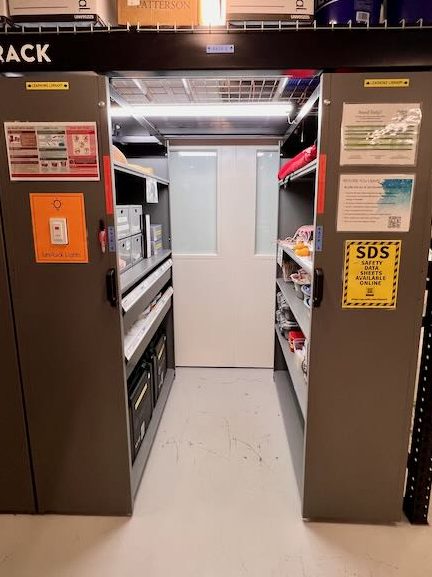 Looking into the first two racks of the Levrack system. There are several shelves on each side, and lots of task trainers and supplies visible on them.