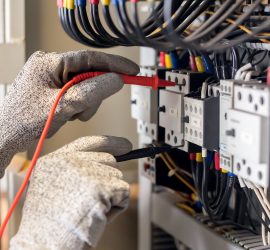 Electrician engineer uses a multimeter to test the electrical installation and power line current in an electrical system control cabinet.