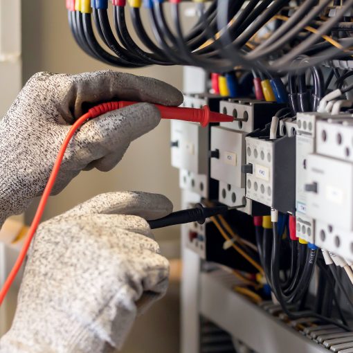 Electrician engineer uses a multimeter to test the electrical installation and power line current in an electrical system control cabinet.