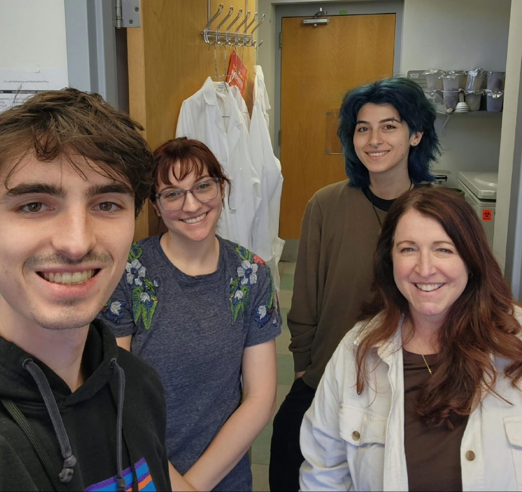 Front-facing photo of the Yi-Pin Lin Lab. Connor is in front, holding the camera. In the background from left to right: Miranda, Carly and Loranne